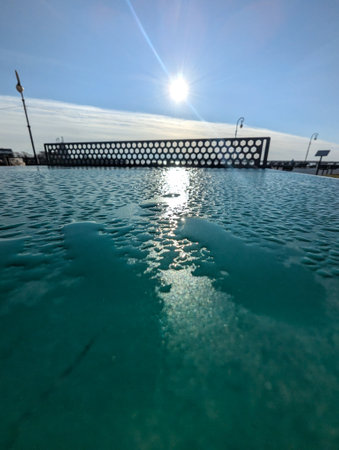 A serene pool reflecting sunlight, featuring a modern structure in the background under a clear sky.の写真素材