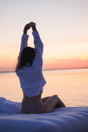 A serene moment captured at sunset, showcasing a person stretching peacefully on a floating platform by the water, embodying tranquility and relaxation.の写真素材
