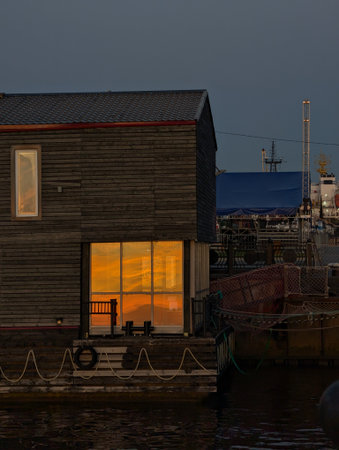 A tranquil scene featuring a houseboat illuminated by warm light at dusk, reflecting on calm waters, creating a serene atmosphere.の写真素材