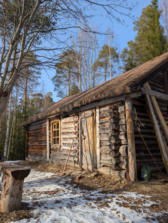 A charming log cabin nestled among trees, showcasing rustic architecture in a serene winter setting with patches of snow.の写真素材