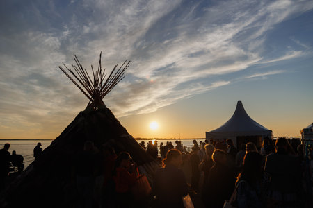 People are joyfully enjoying a vibrant and breathtaking sunset during a lively cultural gathering near the waterの写真素材