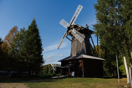 A stunning windmill stands proudly tall in a calm and serene landscape framed by lush trees beneath...