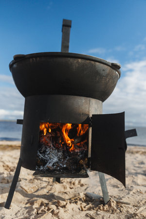 A classic cooking pot positioned over a glowing open flame, set against a beautiful and scenic beach backdropの写真素材