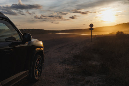 A car is parked on the side of a rustic dirt road as the stunning sunset casts beautiful colors...