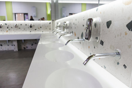 Modern restroom sinks with wallmounted chrome faucets on a speckled terrazzo countertop bright...