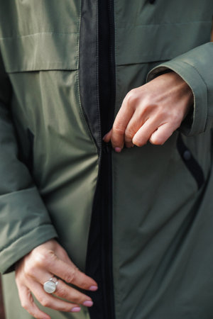 hands latch winter coat, intimate scene of fingers carefully closing jacket zipper in cold outdoor