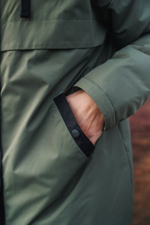 individual resting during autumn walk outdoors, closeup of hand in olive jacket pocket on trail