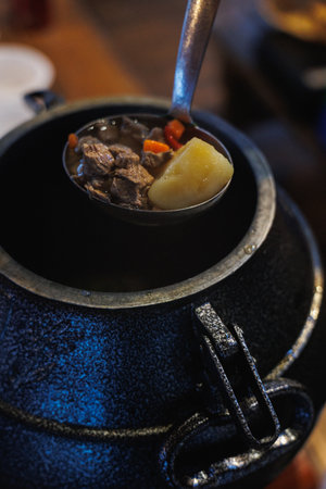 Ladle Steaming Stew Over Cauldron Tender Beef Cubes Potato Carrot Amber Broth Rustic Iron Pot...