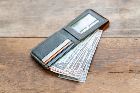 Close-up of a brown leather wallet with dollar bills and credit card on a wooden table.の写真素材