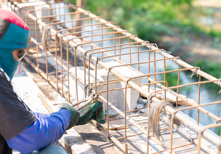 A worker uses steel tying wire to fasten steel rods to reinforcement bars for make fence.の写真素材
