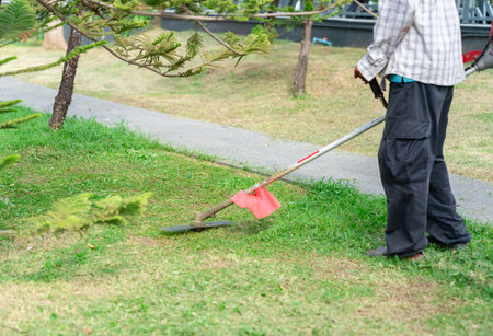 A worker operates a lawn mower while cutting grass in a small public garden.