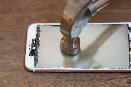 Close up of crash mobile phone smash by rusty iron hammer on wooden table.の写真素材