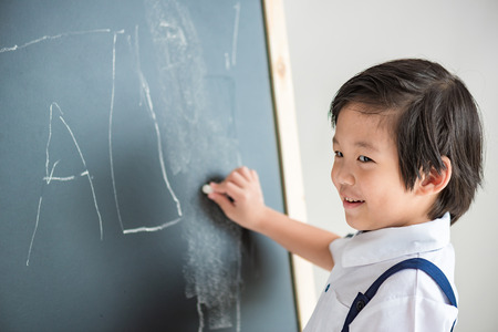 Close up of smart asian boy in white shirt try to writing on the wooden blackboard.の写真素材