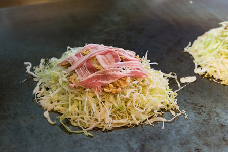 Close up of japanese local food called okonomiyaki or hiroshima pizza cooked by mixed cabbage,pork.noodle.egg and sauce on iron plate in osaka Japan.の写真素材