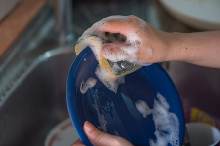 Close up of hand washing ceramic dish in sink.の写真素材