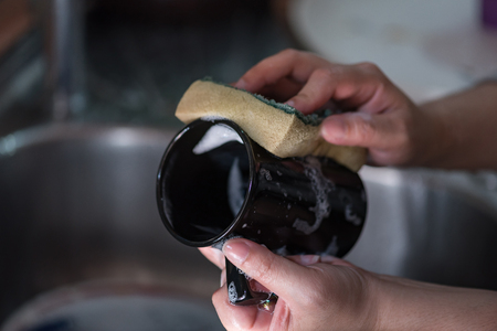 Close up of hand washing black ceramic coffee cup in sink.の写真素材