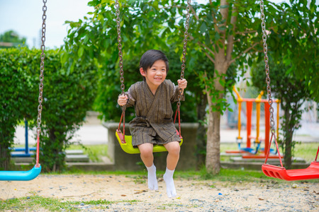 Close up of happy asian boy wear japanese cloth playing swing in park.の写真素材