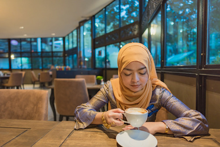 Close up of beautiful muslim woman sit and drinking hot coffee in cafe.の写真素材