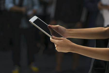 Scene of female hands holding the tablet with the blurred people in the background.