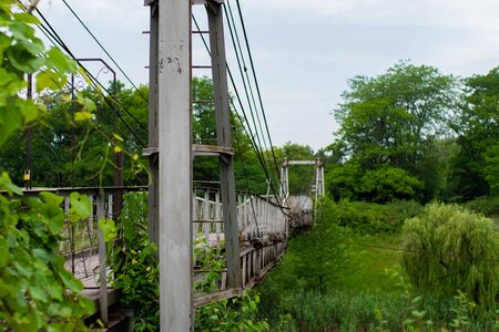 Old iron non-functioning suspension bridge over a dried river side view.