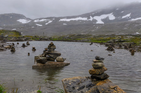 stones over a lake in a fiord in norway with snow on the top of the mountainsの写真素材
