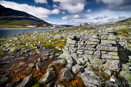a rock construction to keep fresh the fish next to a glacier lake from melted snow in Norway and red wooden houses in the backgroundの写真素材