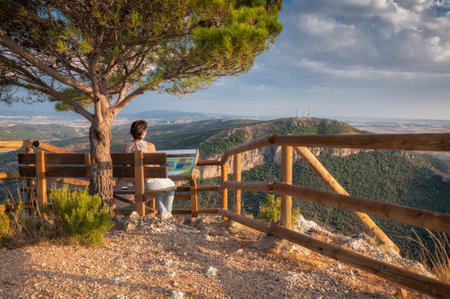 young girl sitting on a bench and looking at the landscape in a viewpoint high in a mountainの写真素材