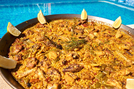 traditional paella with lemon slices decorating next to a swimming poolの写真素材