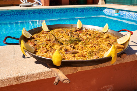 traditional paella with lemon slices decorating next to a swimming poolの写真素材