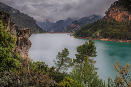 water reservoir surrounded by mountains and cloudy sky in Spain with pine trees on the imageの写真素材