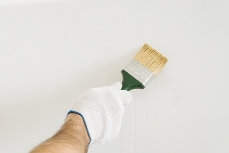the brush in his hand in a white glove against a light wallの写真素材