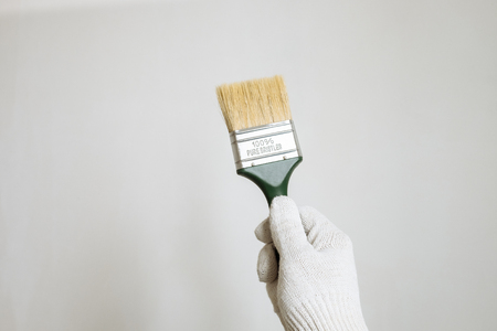 the brush in his hand in a white glove against a light wallの写真素材