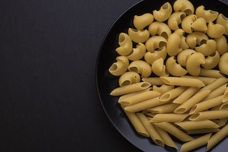 raw pasta on the black  plate on black background and place for inscription