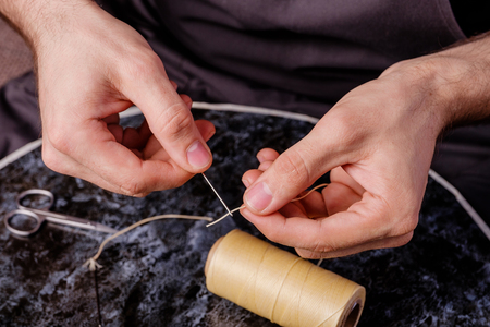 leather needle and waxed thread in men's hands, tools used by shoemakers close up