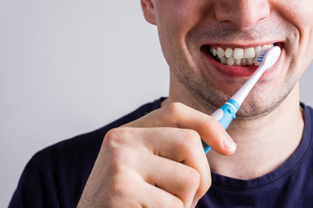 man cleaning teeth with electric toothbrush closeupの写真素材