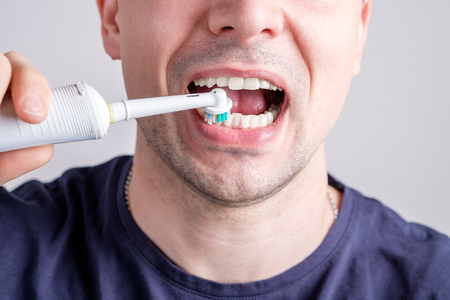 man cleaning teeth with electric toothbrush closeupの写真素材