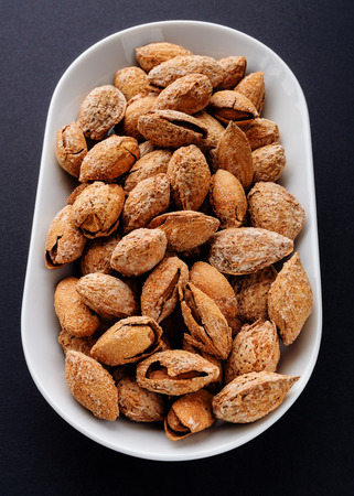 salted almonds in shell on white plate on black slateの写真素材