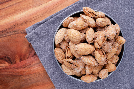 nuts snack salted almonds in shell in metal plate on dark grey linen napkin on wooden table top viewの写真素材
