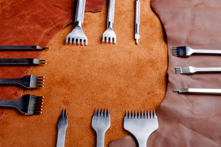 leather-working tools on natural brown leather background, in workshop, copy space for text in centerの写真素材