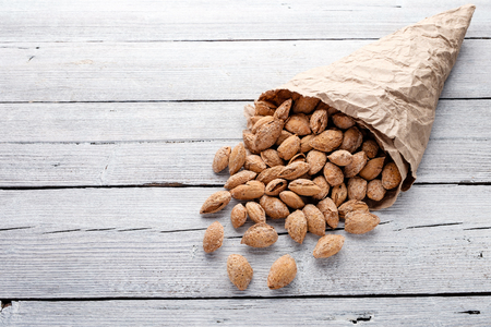 salted almonds in shell in paper bag on white wooden background closeupの写真素材