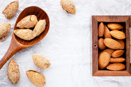 box is mahogany with nuts snack salted almonds and brown wooden spoon on white baking paper top viewの写真素材