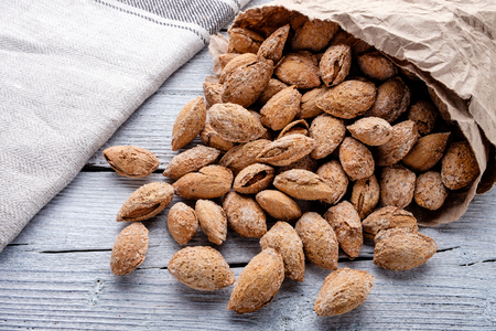 salted almonds in shell in paper bag on white wooden background closeup, linen napkinの写真素材