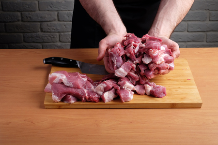 man in the black apron cuts of pork or beef on a cutting wooden board in the kitchenの写真素材