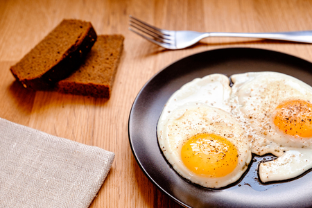 two fried egg with black pepper on black plate on wooden tableの写真素材