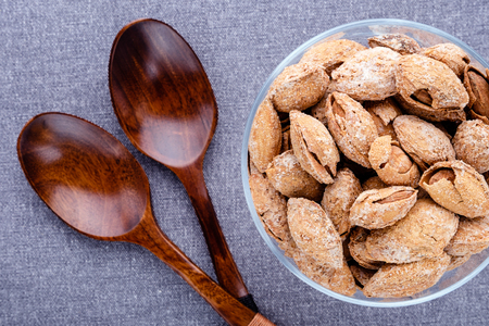 almond on glass plate and brown wooden spoon on dark grey linen napkin background , top view.の写真素材