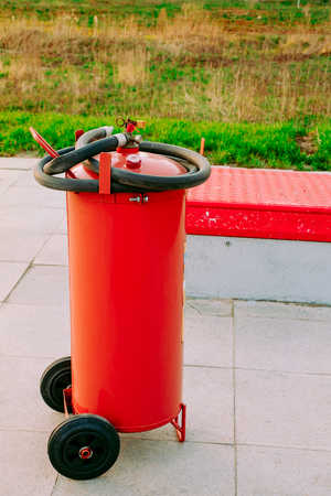 big red fire extinguisher on wheels with a black hose at auto gas stationの写真素材