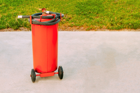 big red fire extinguisher on wheels with a black hose on a concrete floorの写真素材