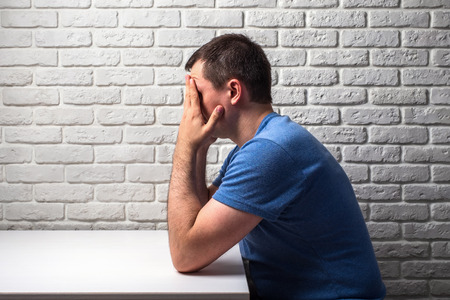 man in stress holds his head with his hands sitting at the white deskの写真素材