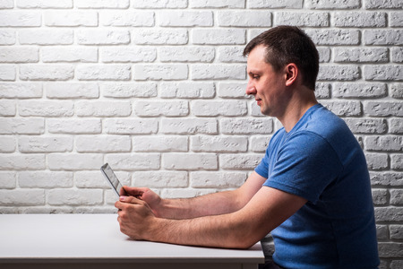 Male browsing the web on his tablet at white tableの写真素材