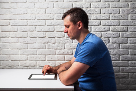 Male browsing the web on his tablet at white tableの写真素材